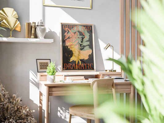 Sunlit home office with wooden desk, chair, potted plant, and Queer and Dramatic wall art with colorful, flowing illustration. Shelf above holds books and decorative items.