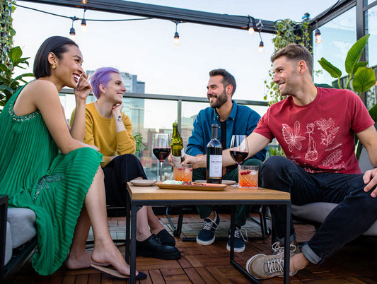 A diverse group sitting together at a rooftop patio are engaged in a conversation. The environment is modern, with plants and natural light that conveys comfort, curiosity, and emotional connection.