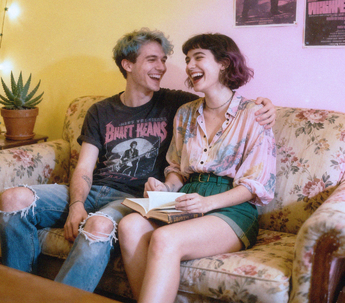 A joyful, non-normative couple embraces, wearing colorful outfits in a cozy living room. They are smiling and laughing, radiating happiness and affection.