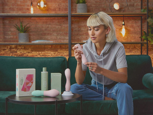 A woman in a cozy living room sits on a green velvet couch looking different choices of toys - for pleasure centered lifestyle and self-discovery