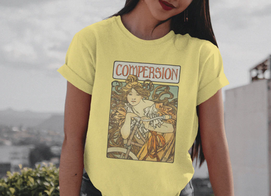 A woman in a bright T-shirt stands outdoors with a city backdrop. The shirt features an Art Nouveau-style illustration labeled "Comperision," for ENM and polyamory visibility in style.