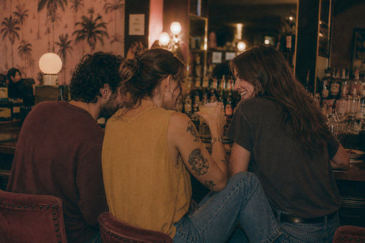 Three friends enjoying drinks at a bar, laughing and chatting together. 
