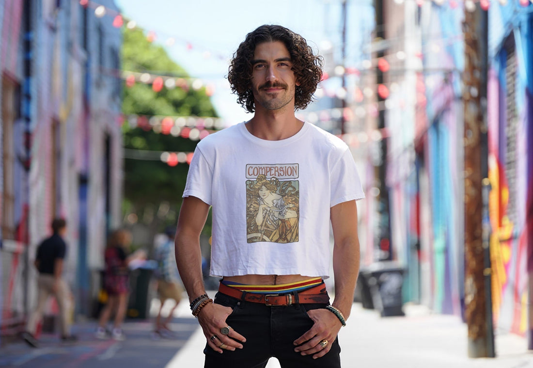 Man confidently wearing a crop top, smiling and posing in front of colorful city alley