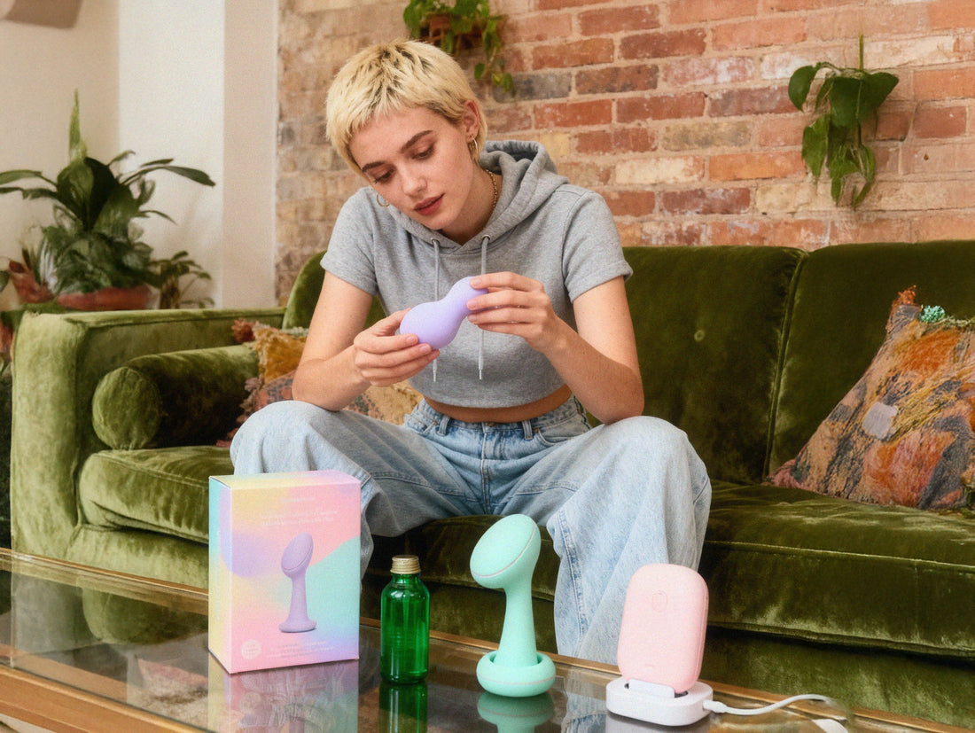 A woman in a cozy living room sits on a green velvet couch looking different choices of toys - for pleasure centered lifestyle and self-discovery