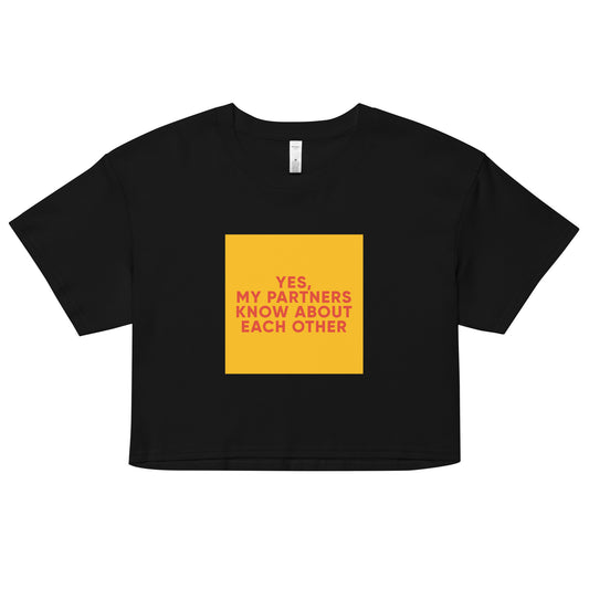 Black cropped tee with bold orange-red text reading “Yes, My Partners Know About Each Other,” cheeky ENM-affirming statement top for open-relationship style.
