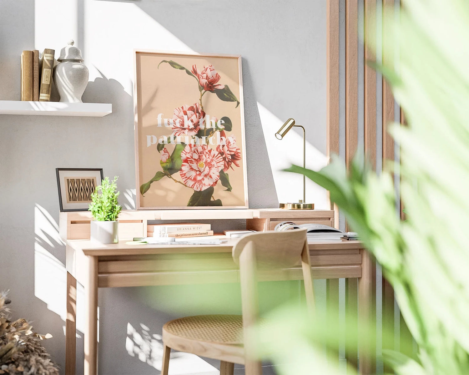 Sunlit home office with wooden desk, chair, potted plant, and feminist vintage poster reading "Fck the patriarchy". Shelf above holds books and decorative items.