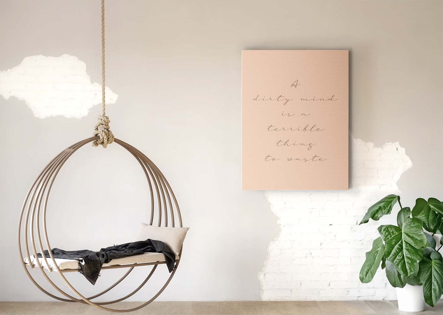 Hanging chair with cushion and blanket, beside a stylish pink wall artwork with a humorous and empowering message. A green plant sits on the floor, adding a cozy vibe.