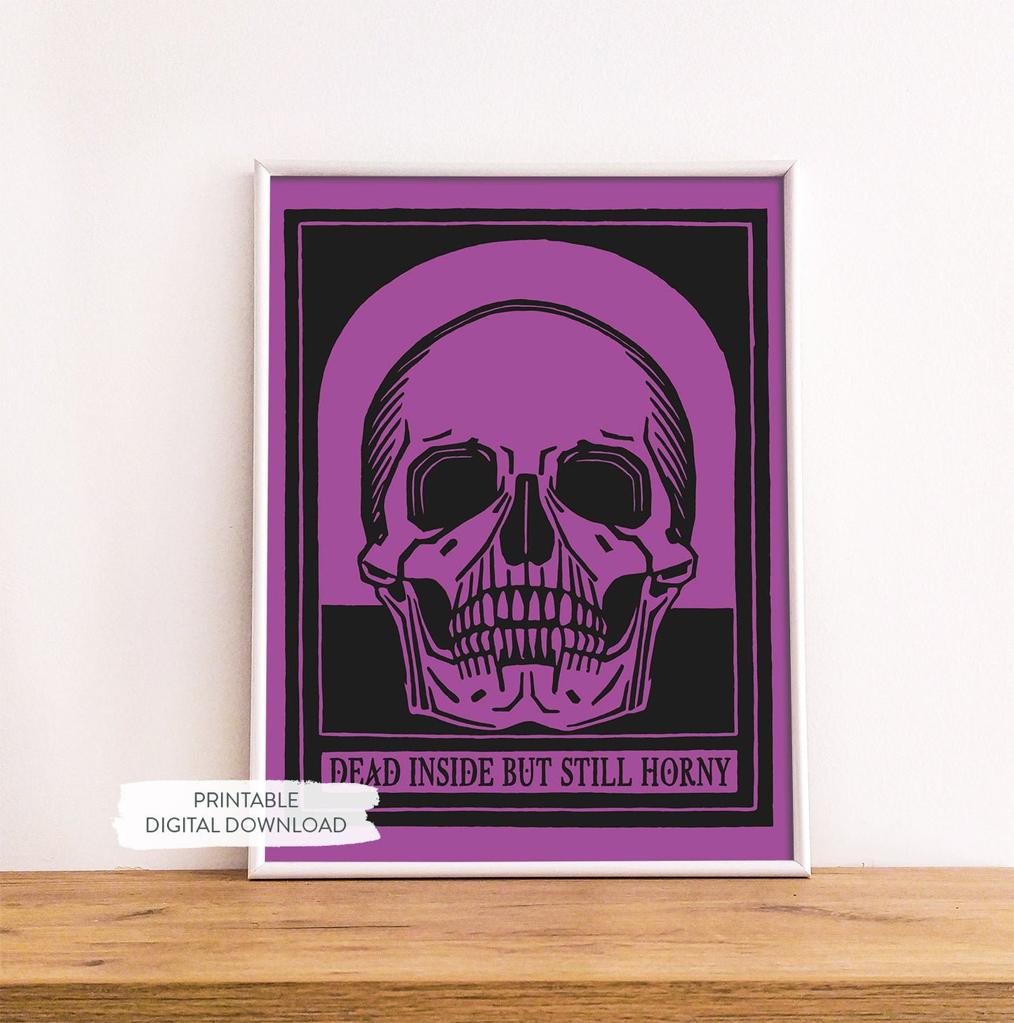 With frame on a wooden shelf with a printable poster featuring a skull with the phrase 'Dead Inside But Still Horny' on a purple background.