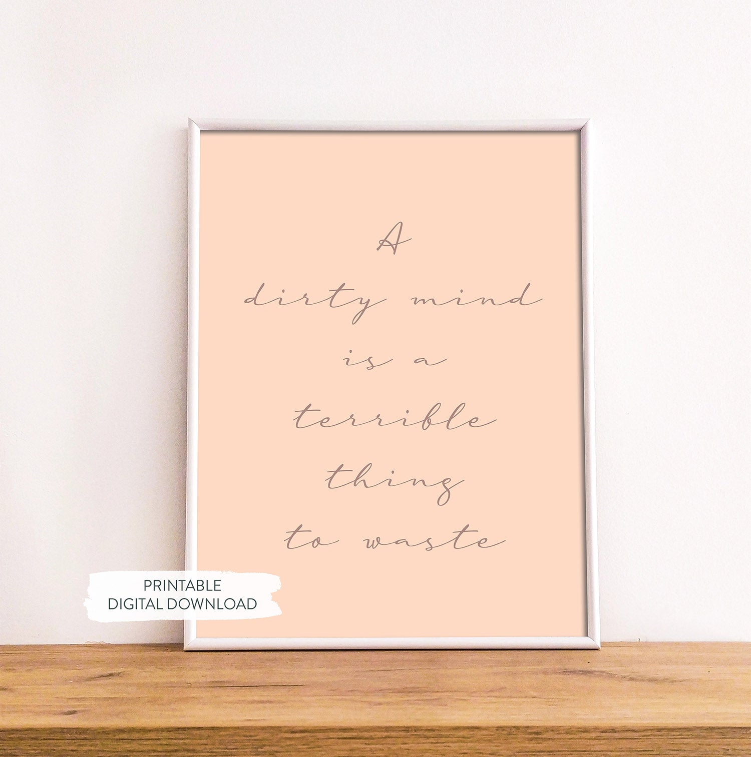 Sex-positive wall art featuring bold white text on a pink background shown in white frame on wood shelf