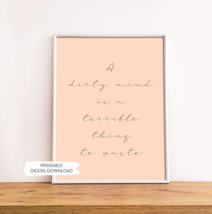 Sex-positive wall art featuring bold white text on a pink background shown in white frame on wood shelf