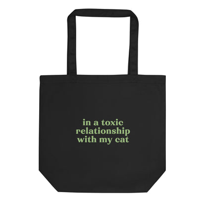 Black eco tote bag with green text saying 'In a Toxic Relationship with My Cat' for cat lovers tired of dating.