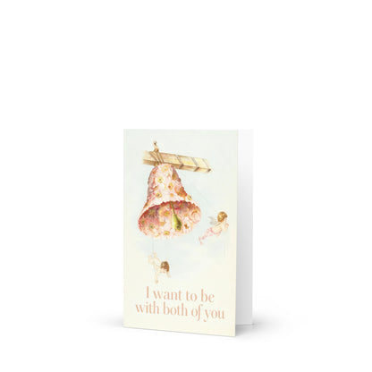 Vintage-style greeting card featuring cherubs floating around a decorative cake, with the text “I want to be with both of you,” celebrating polyamorous and throuple love.