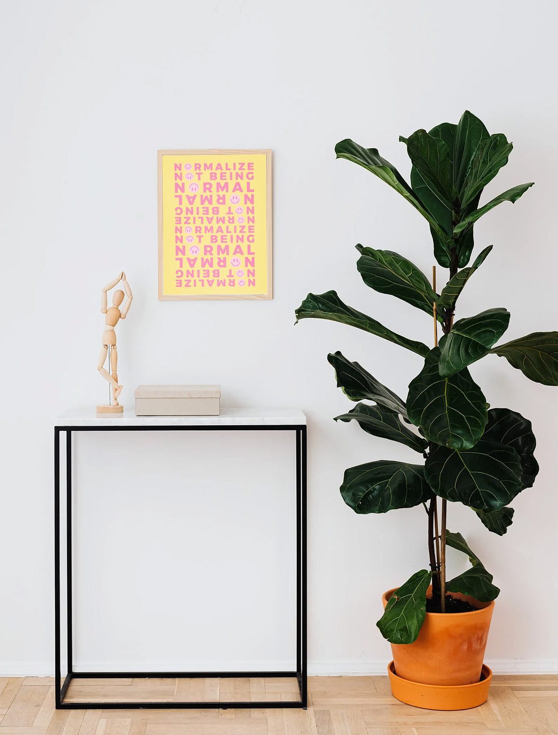 A framed neurodivergent Affirmation Wall Art above a minimalist interior with a tall green plant in an orange pot next to a small black table.