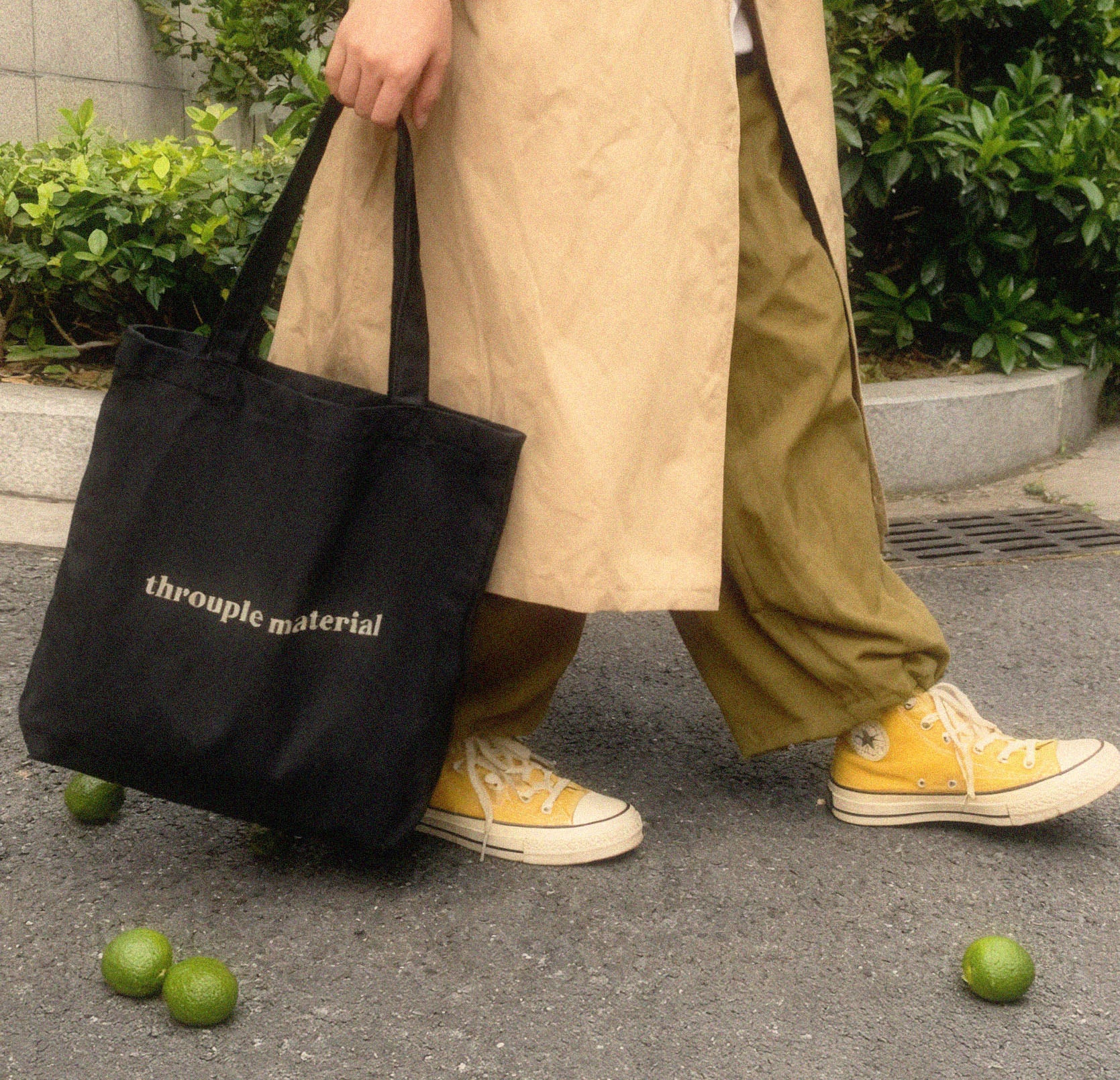 Person holding a black tote bag with 'throuple material' text, for ENM expression and pride with fashion style.