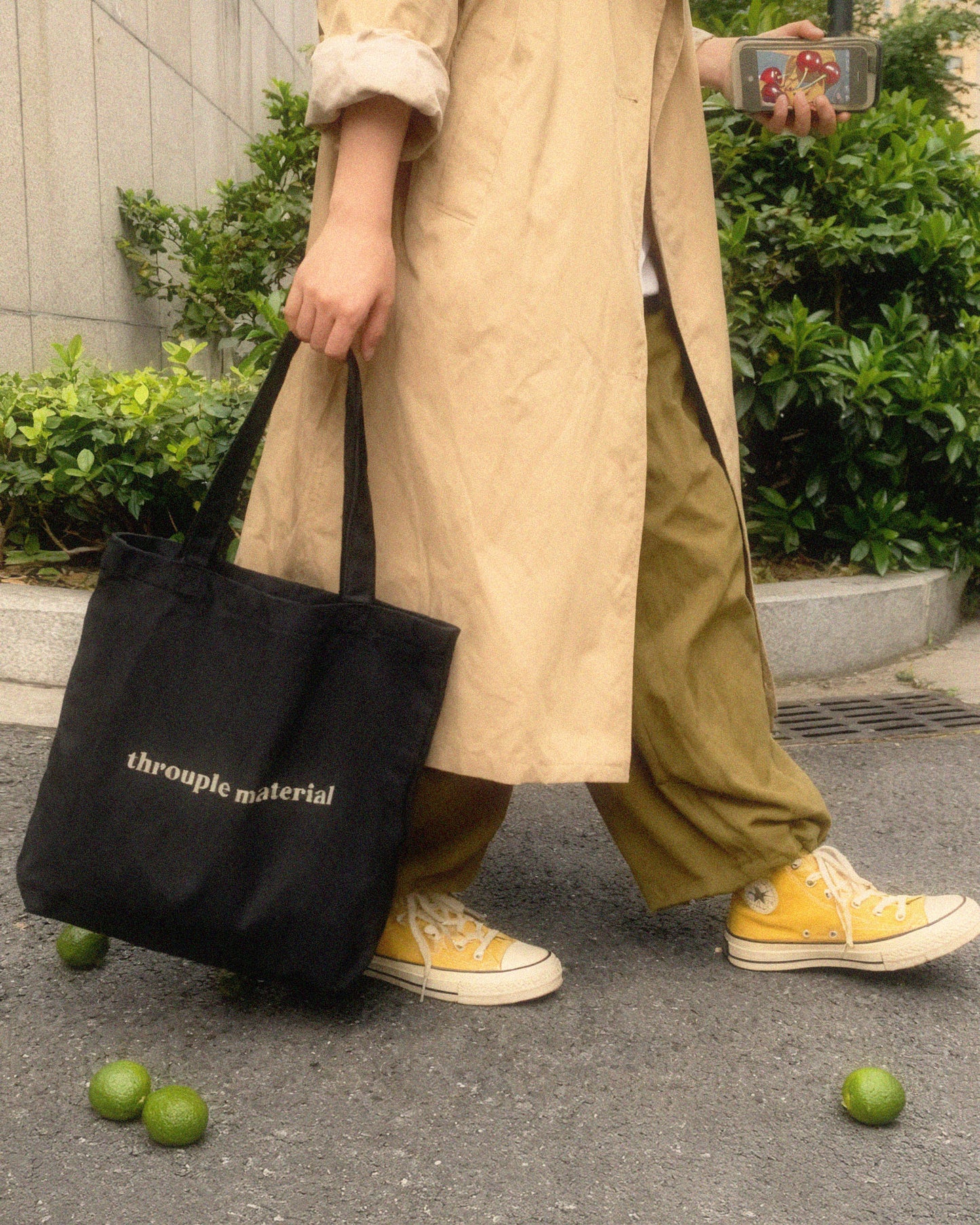Person with slouchy pants and converse shoes carrying a black tote bag with “Throuple Material” text – non-monogamy statement accessory for polyamorous visibility and everyday ENM style