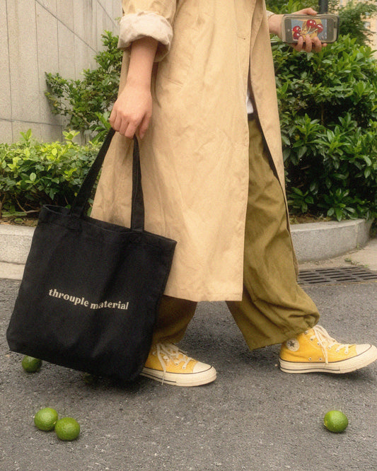Person with slouchy pants and converse shoes carrying a black tote bag with “Throuple Material” text – non-monogamy statement accessory for polyamorous visibility and everyday ENM style