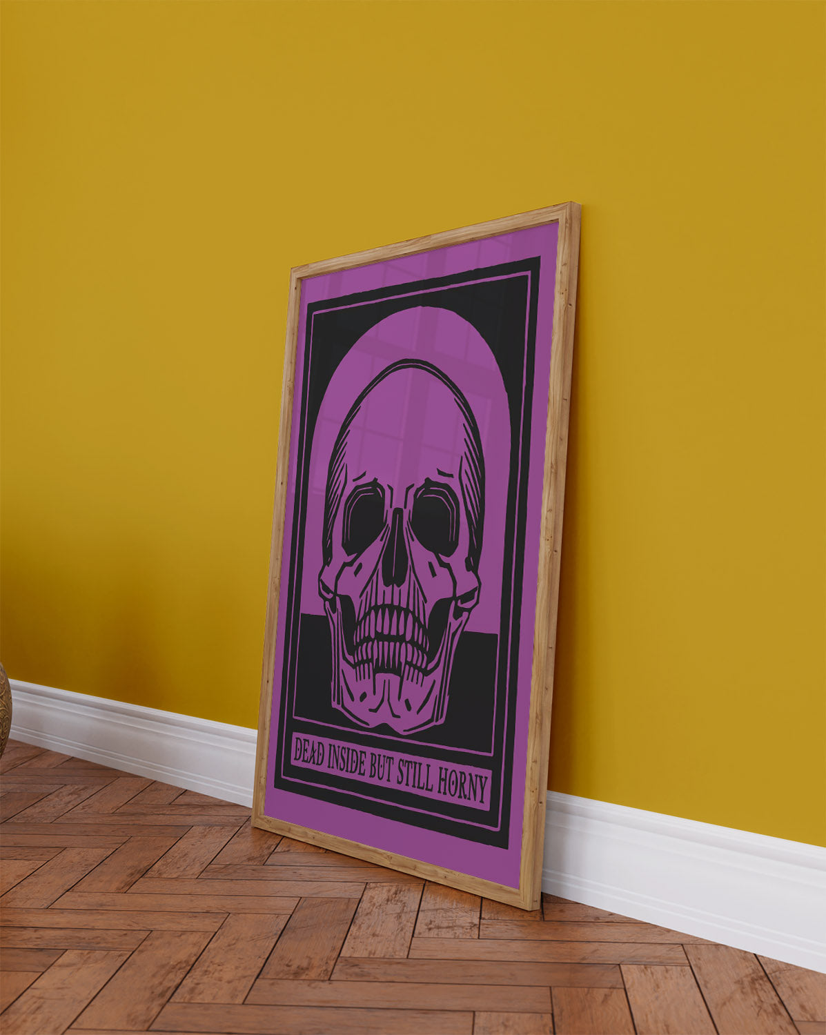 Framed bold skull art poster with purple and black color scheme leans against a colorful wall on a wooden floor.