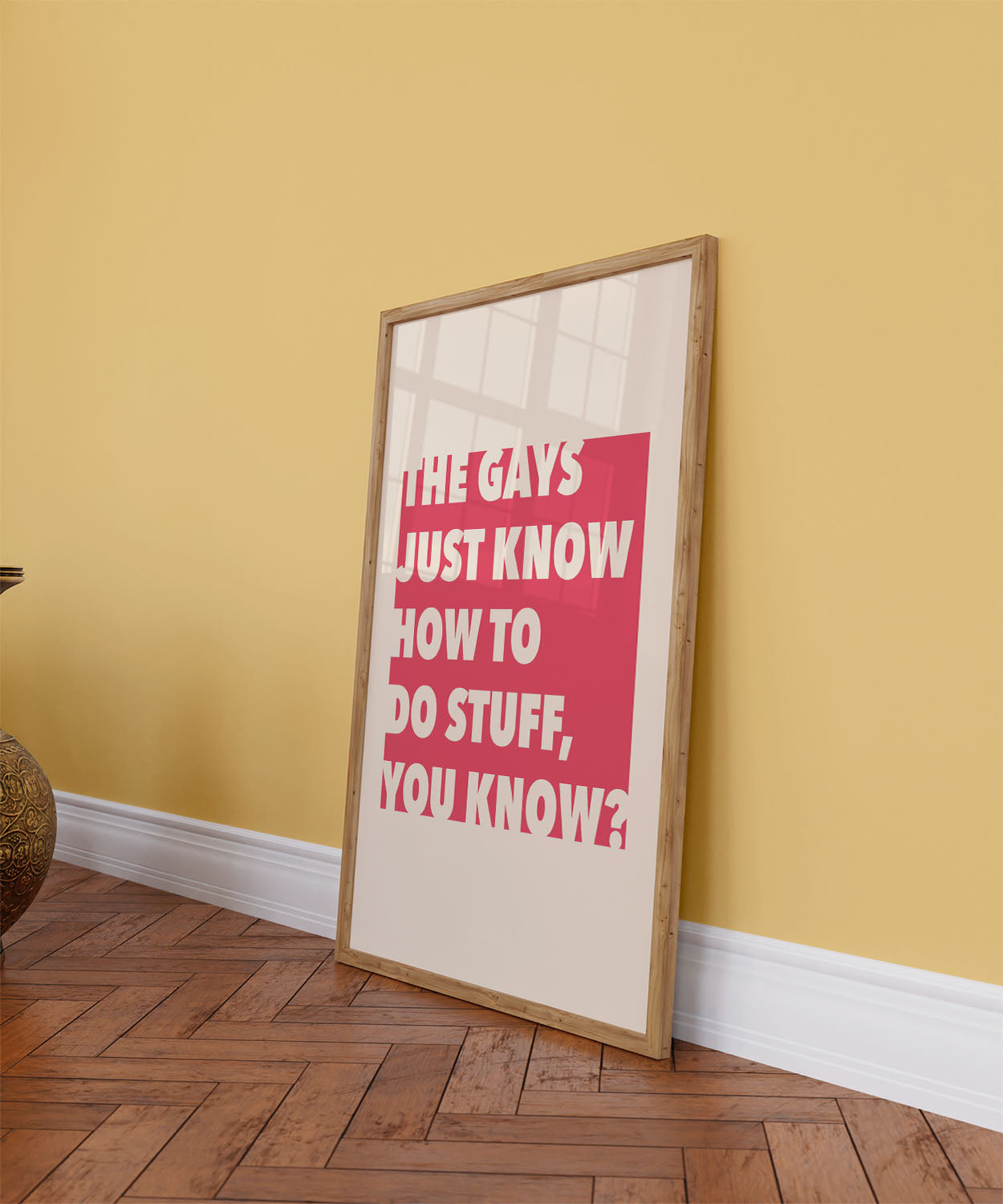 Framed queer printable wall decor with bold red background leans against a colorful wall on a wooden floor.