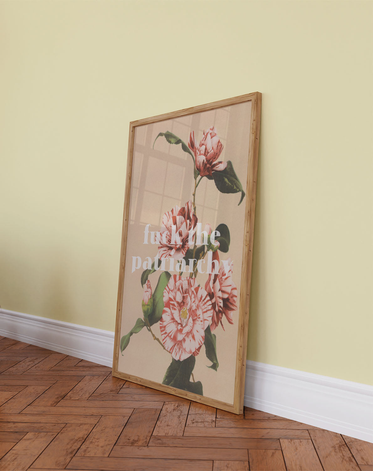 Bold vintage feminist poster with flowers and the print "Fck the patriarchy" leans against a light yellow wall on a wooden floor.